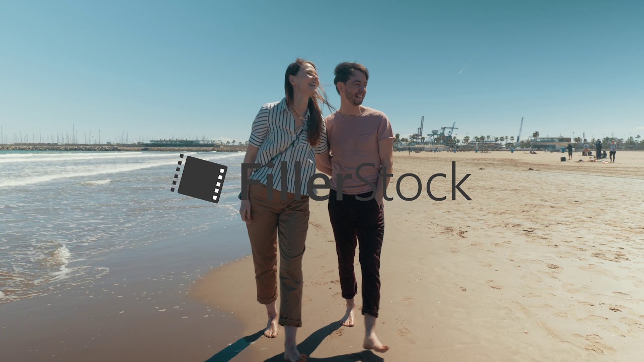 A happy couple walking down the beach barefoot holding hands