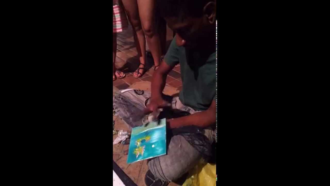 Artista de rua faz pintura em azulejo com os dedos e palito de dente.
