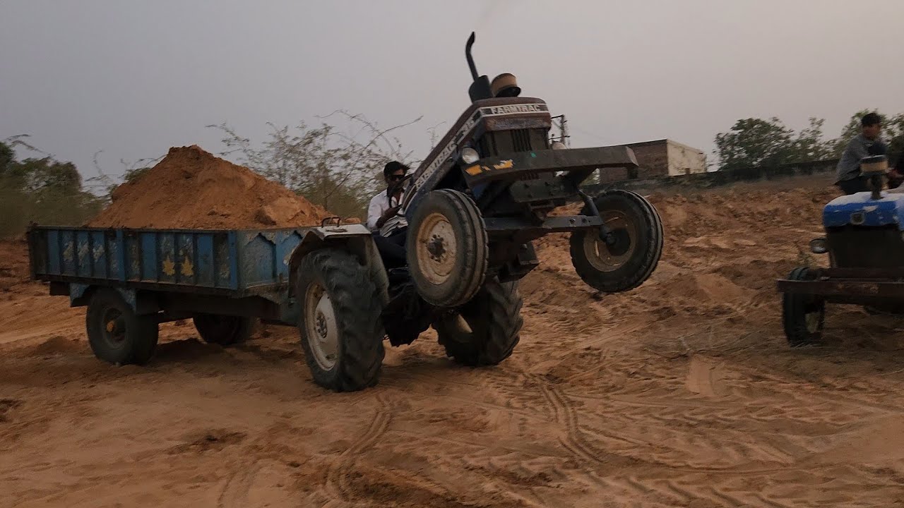 Farmtrac , John Deere,  New Holland, tractor pulling a trolley fully loaded with sand.