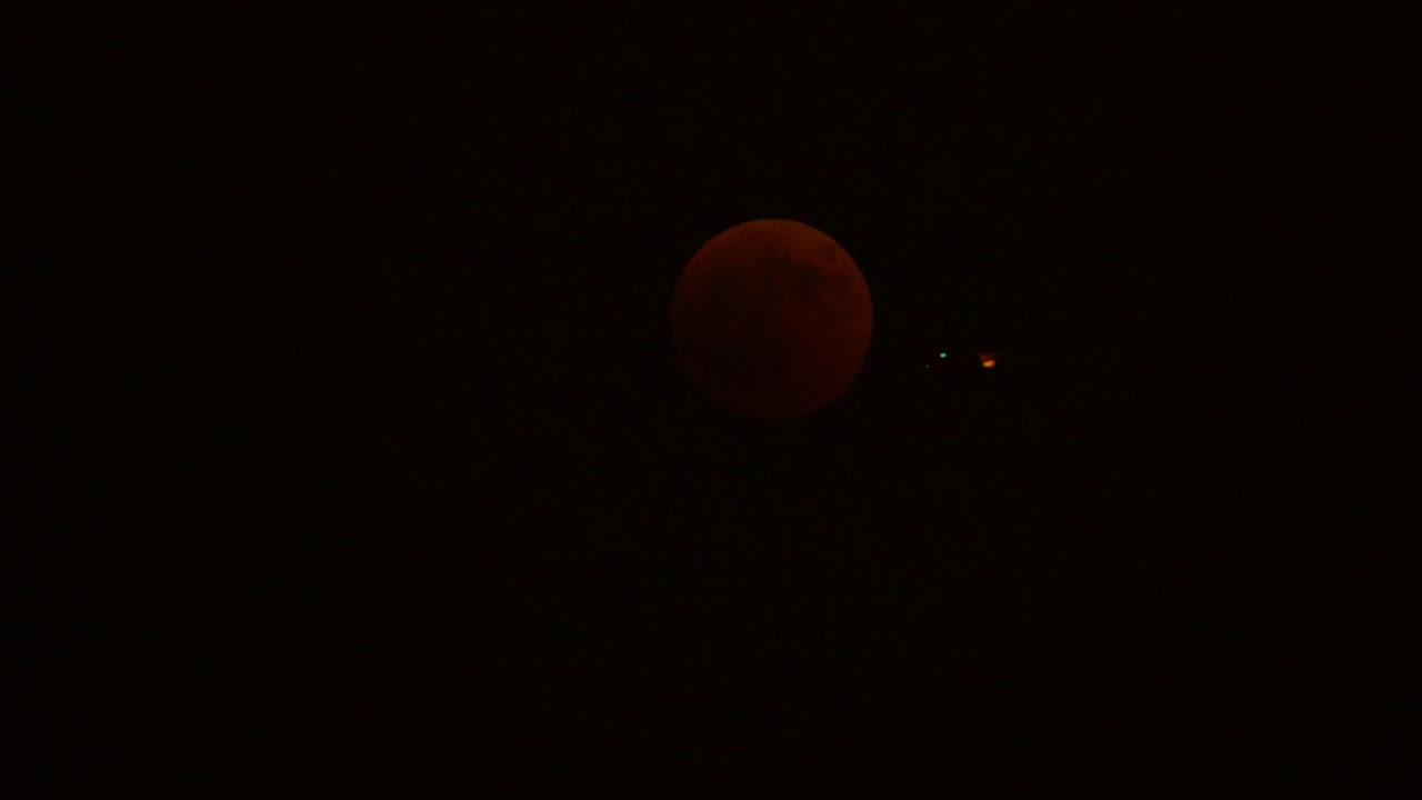 Aeroplane flying in front of a total lunar eclipse, also called a Blood Moon, Barcelona