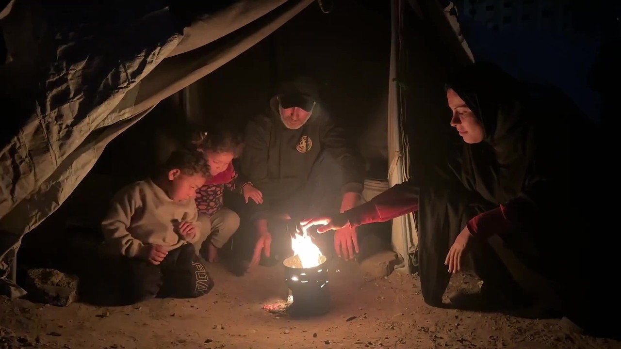 عائلة فلسطينية تشعل النار أمام خيمتها لتدفئة أطفالها في مدينة غزة وسط برد قارس
