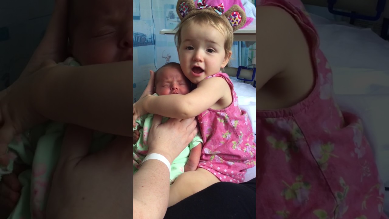 Cute toddler holds baby sister for the first time