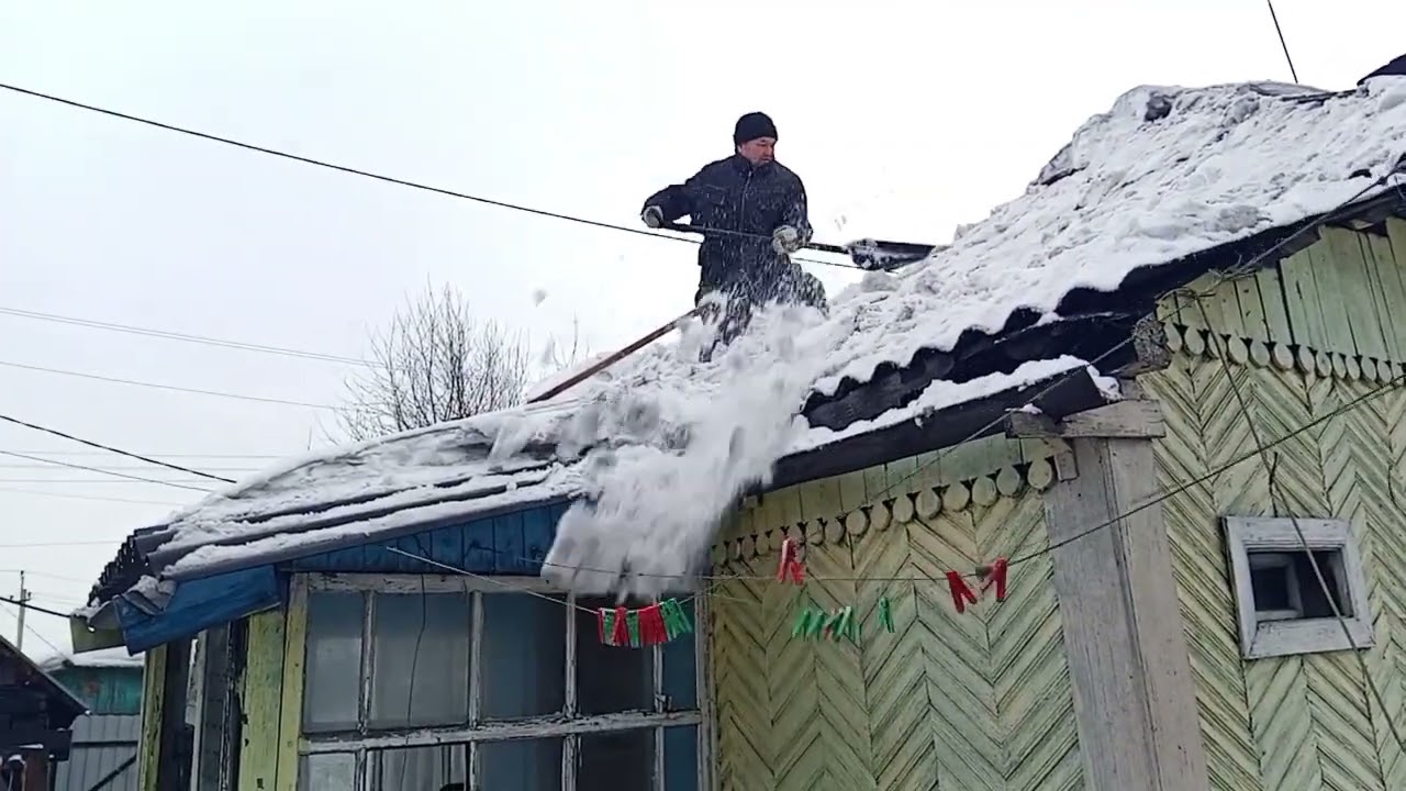 Зимний труд: чистка снега с крыши дома
