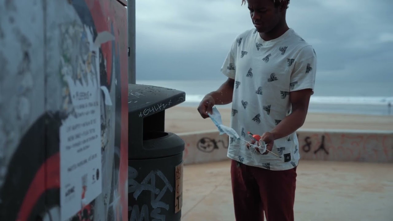 A man throwing garbage into a trash can on the beach