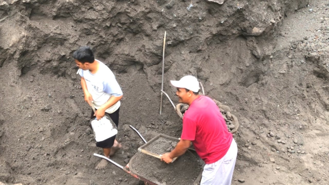 Two miners eagerly sift through the copious amounts of black sand in front of them.