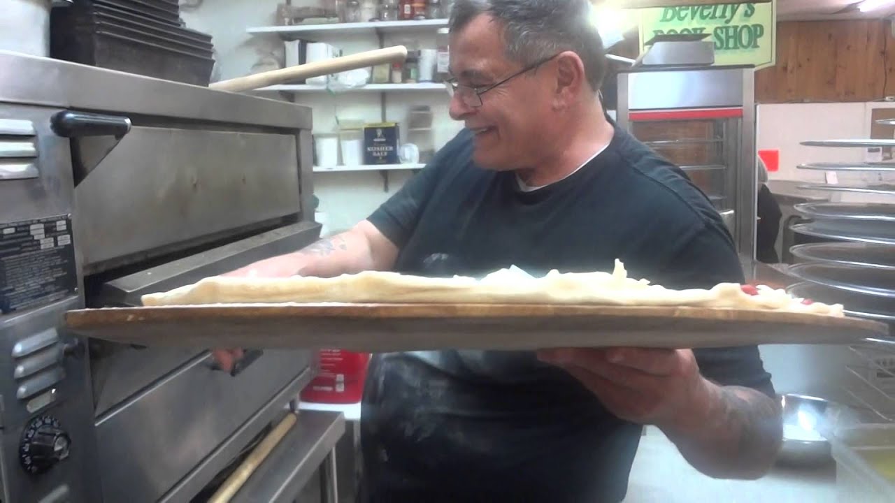Frank Giaquinto slides a pizza into the oven off the handle on a wooden pizza peel