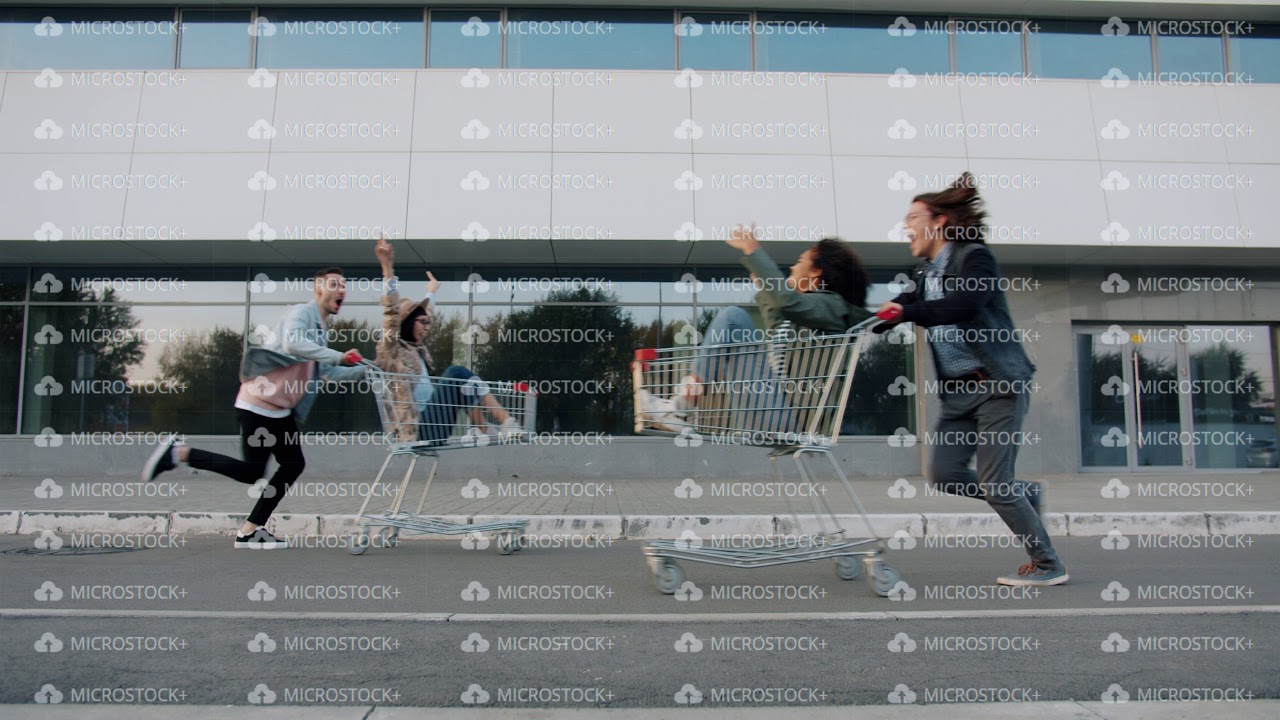 Happy couples riding shoppng carts, men running outdoors pushing trolleys