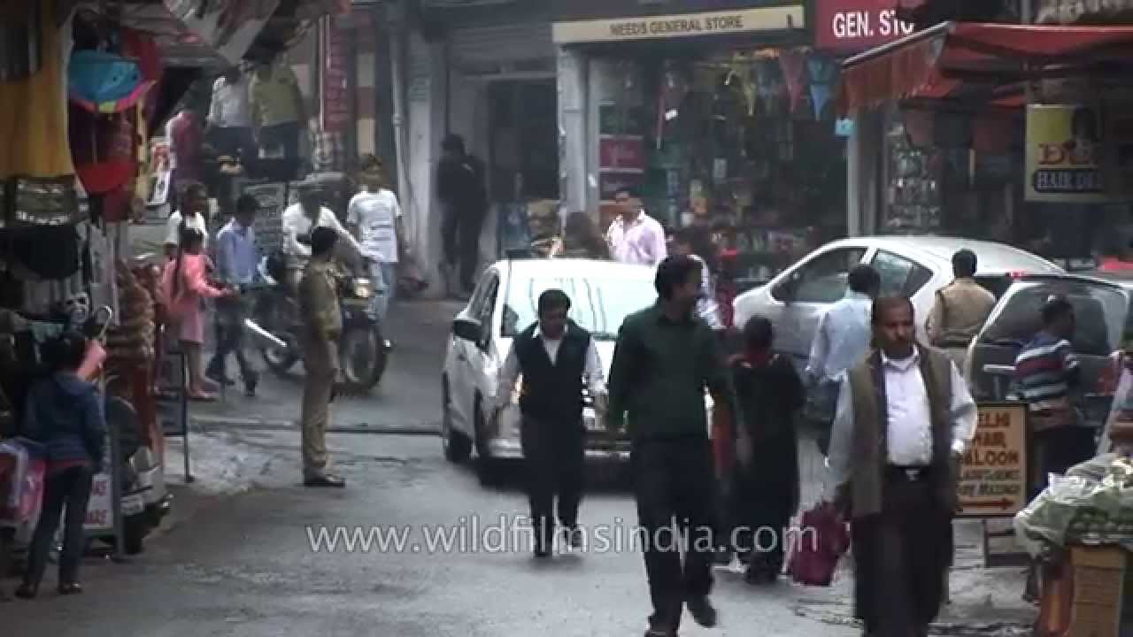 Crowded Mussoorie mall with cars and pedestrians, in monsoon rain