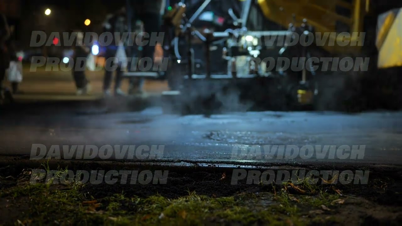 Road roller compacting new asphalt paving at night with steam from hot surface
