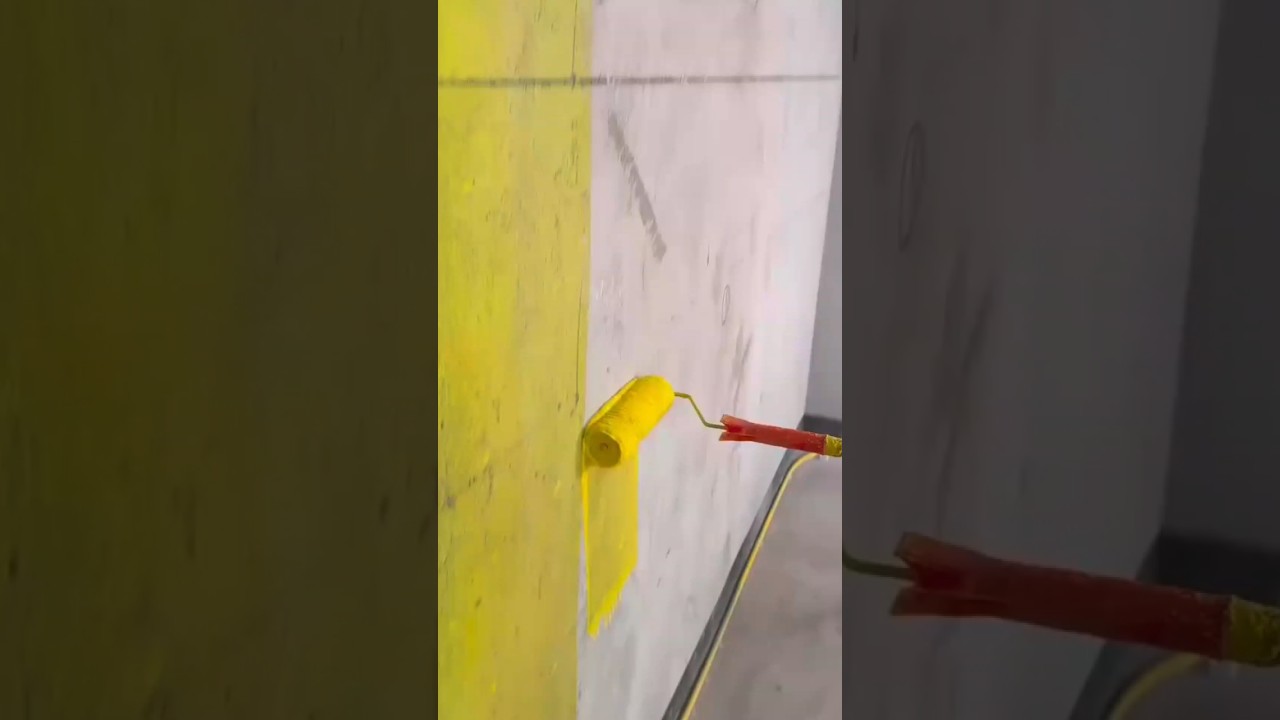 worker uses a paint roller to apply a bright yellow coat to a concrete wall