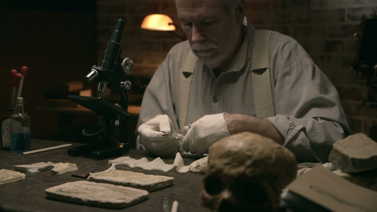A 1930s archeologist in his lab examining an ancient human skull and other artifacts. ASMR
