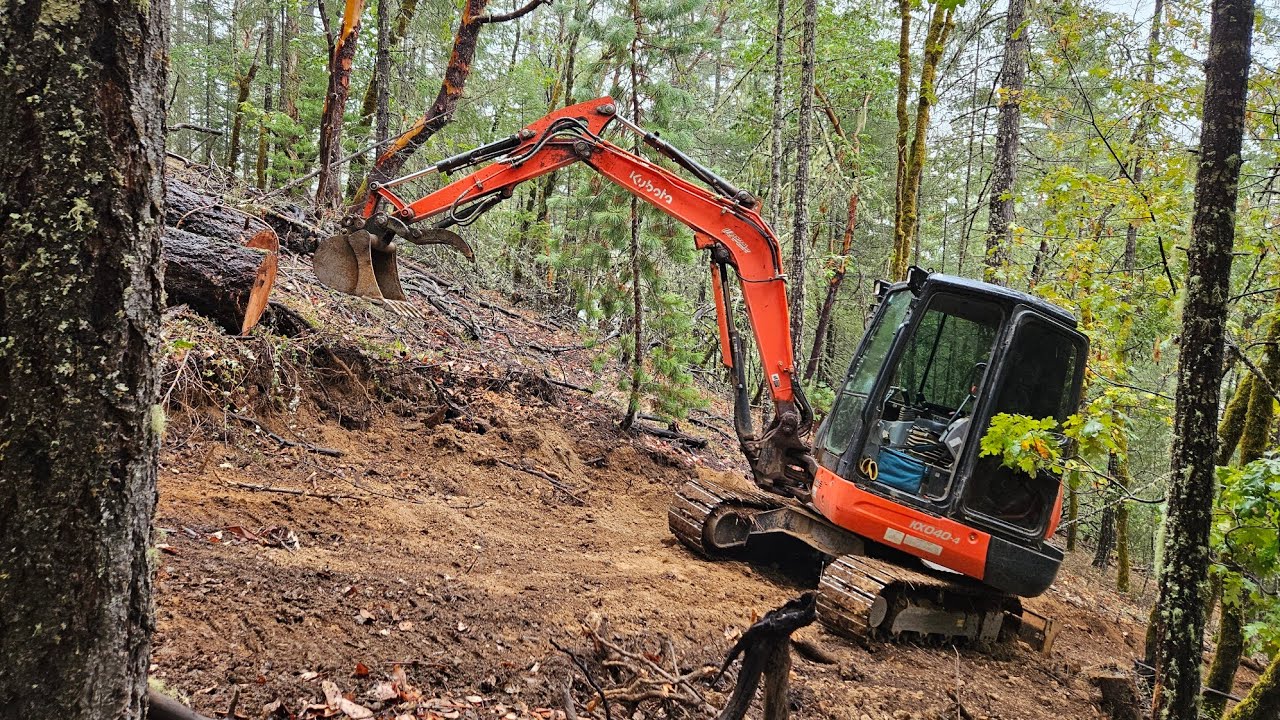 Крутая тропа на склоне холма, за которой гонится бревно, с экскаватором Kubota KX 040 4