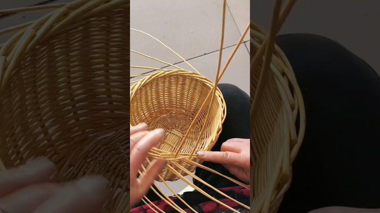 person uses their hands to weave a small, round wicker basket from light reeds