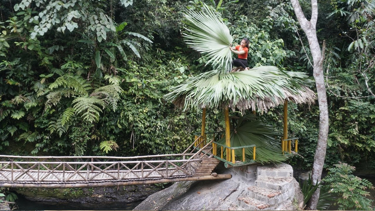 Single girl living in the forest repairs leaf the hut - Green forest farm