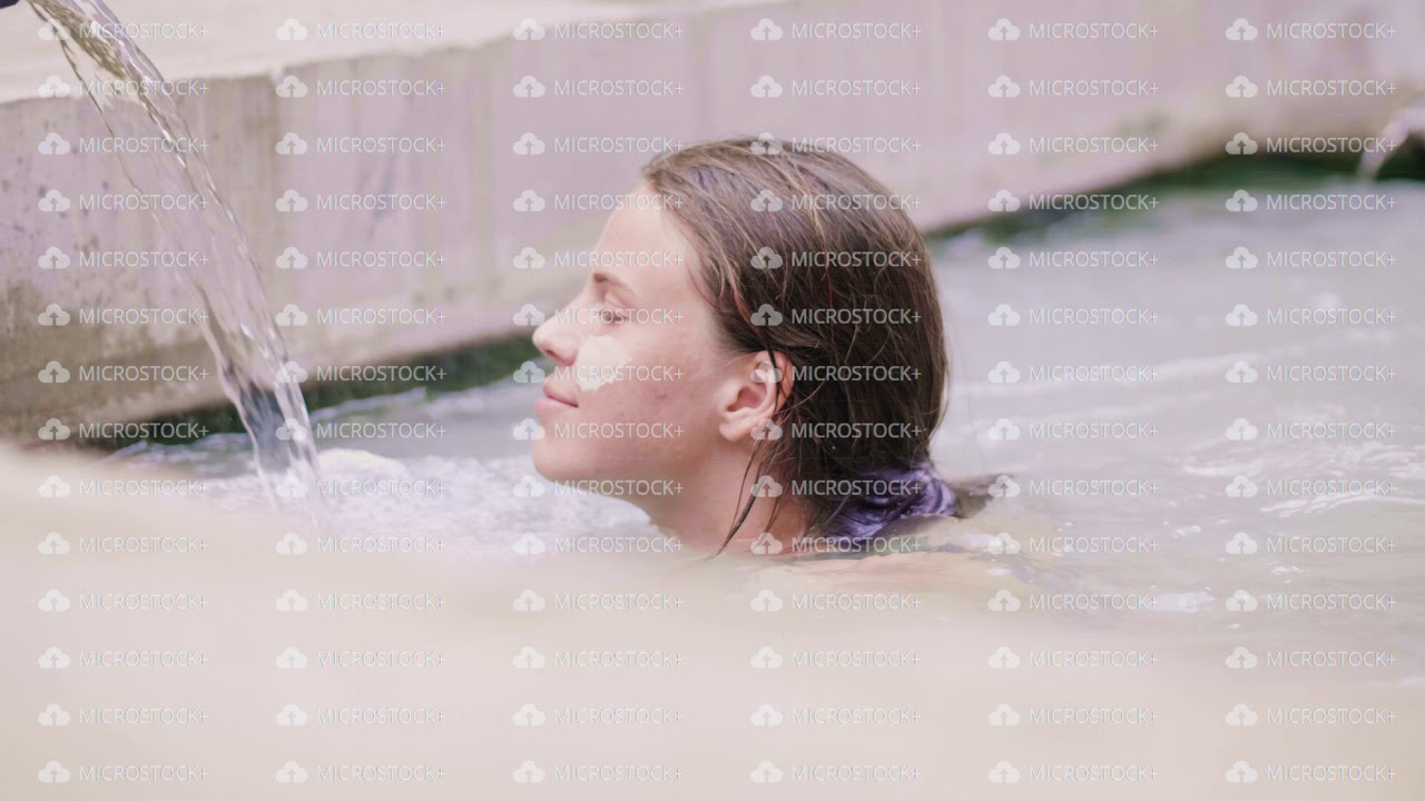 Young woman with mud mask on skin face relaxing in mineral mud in outdoor spa. Beautiful woman