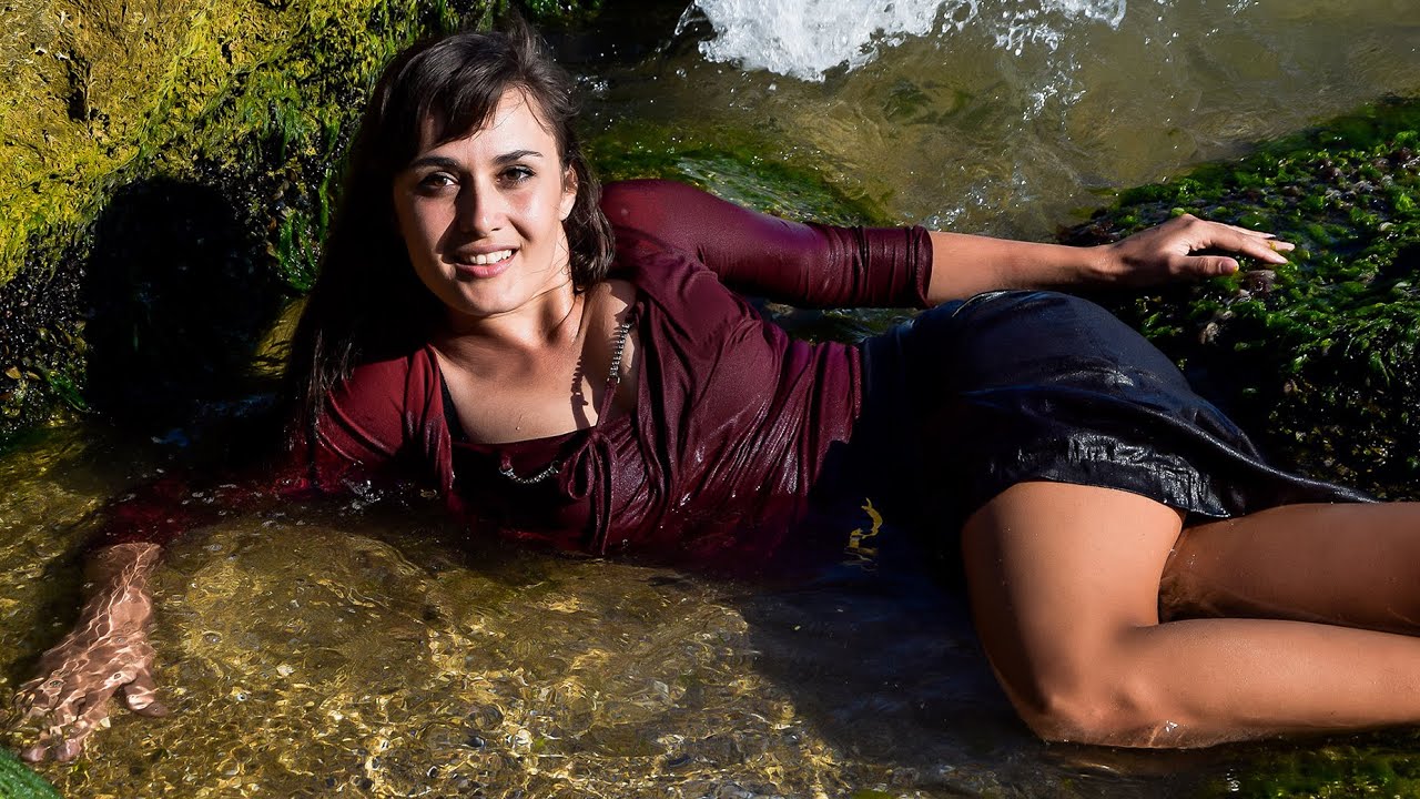 A CUTE GIRL IN WET FORMAL CLOTHES TENDERLY POSE ON THE BEACH BY THE SEA FOR WETLOOK VIDEO