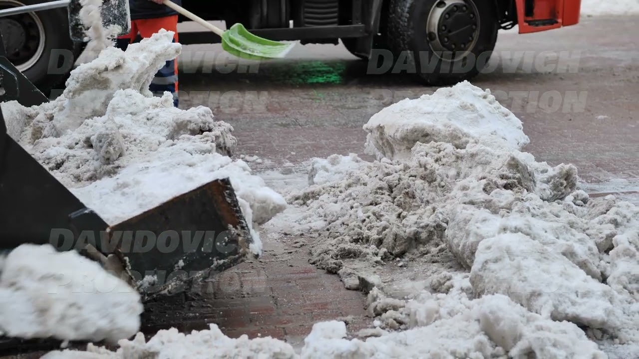 Tractor shovel loading snow and ice into truck during winter road cleaning