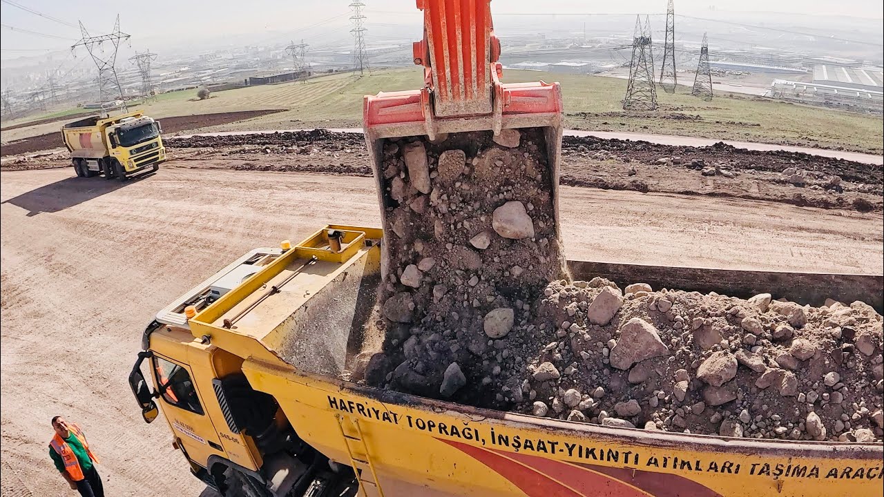 Hitachi Excvator loads stony materials into truck.