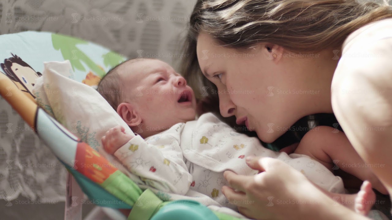 beautiful young mom kiss and soothes cry of newborn baby