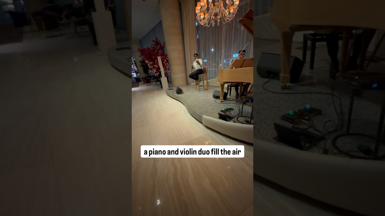 In the bustling lobby a piano & violin duo fill the air with elegant melodies amid the lively crowd.