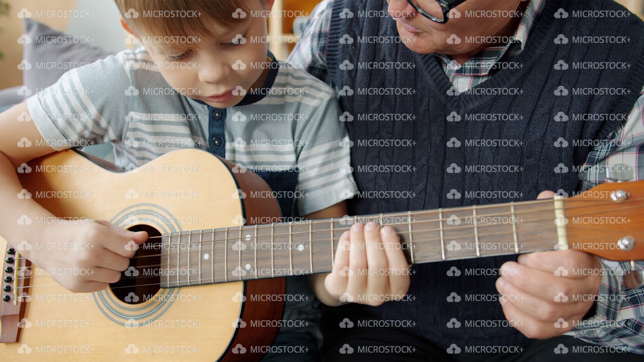 Slow motion of adorable child learning to play the guitar with grandad at home