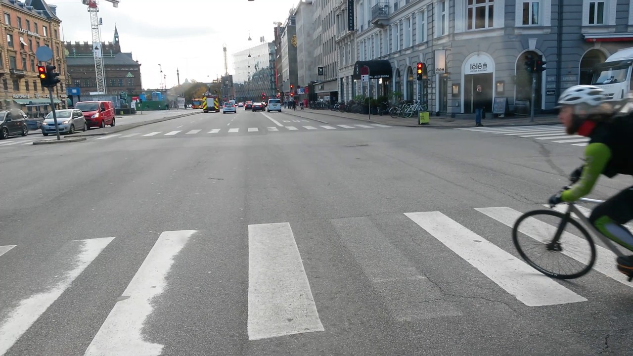 Cykelbud til venstre p&aring; sekssporet vej lige idet lyset skifter
