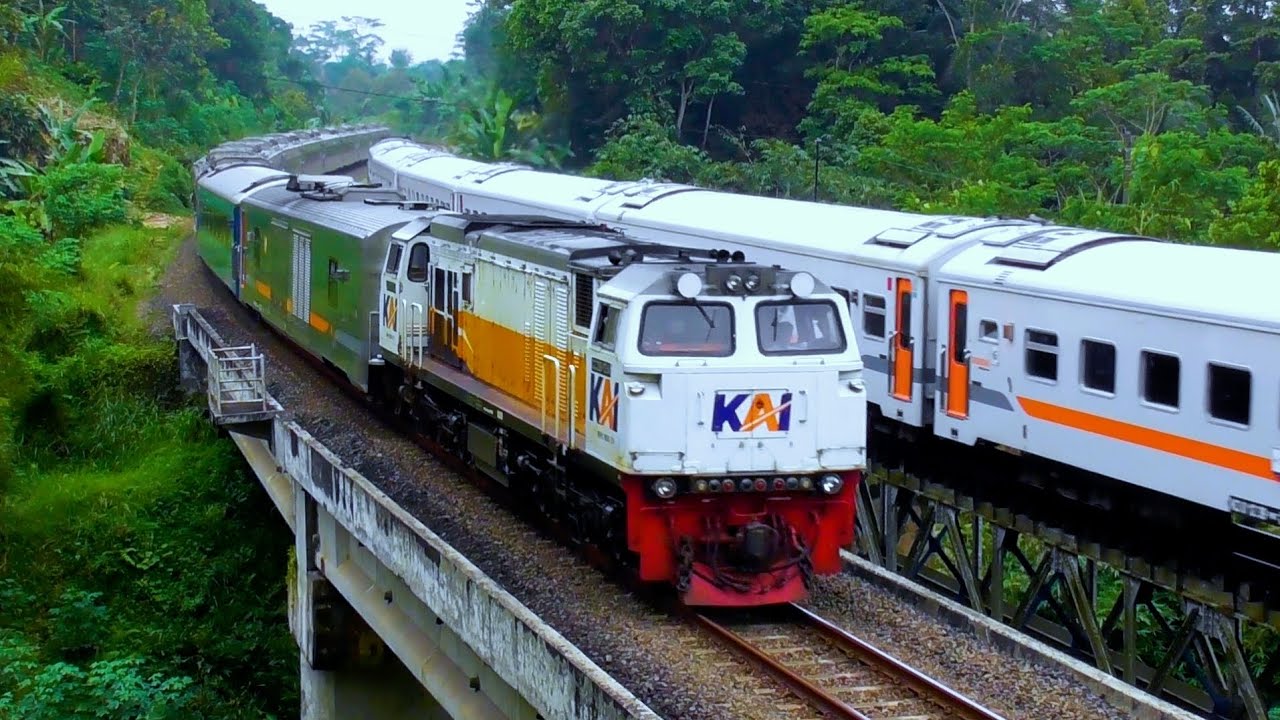 KERETA API PANJANG BERPAPASAN DI ATAS JEMBATAN DENGAN NUANSA PEMANDANGAN DILERENG PERBUKITAN