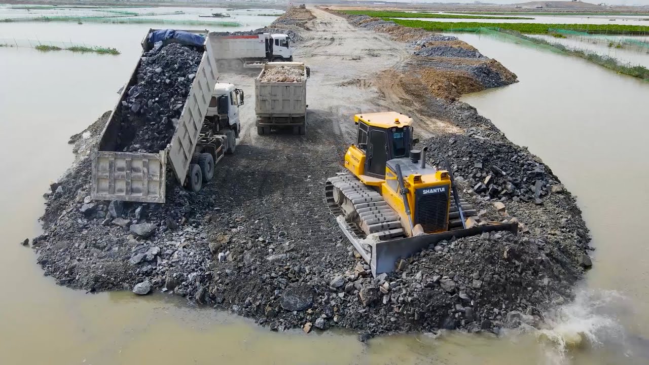 Top activity building causeway with bulldozer company using sand truck to move rocks into the lake
