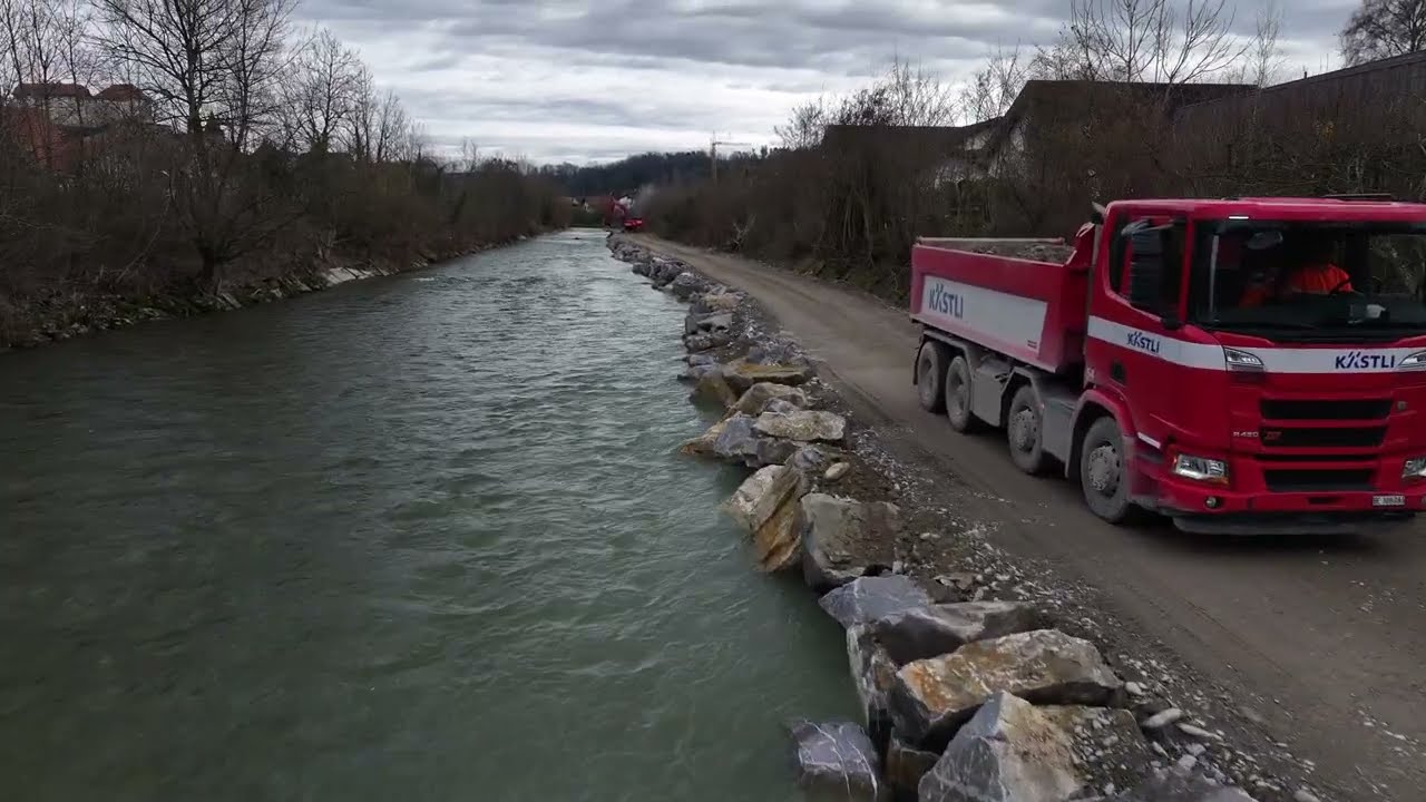 Bau Piste Materialtransport im Flussbett der Sense: Lastwagen mit Kies fährt rückwärts zum Bagger