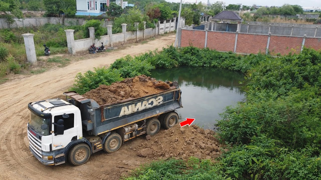 Powerful Komatsu D56E Bulldozer Pushing Landfill With 25Ton Dump Truck pouring soils into pond 