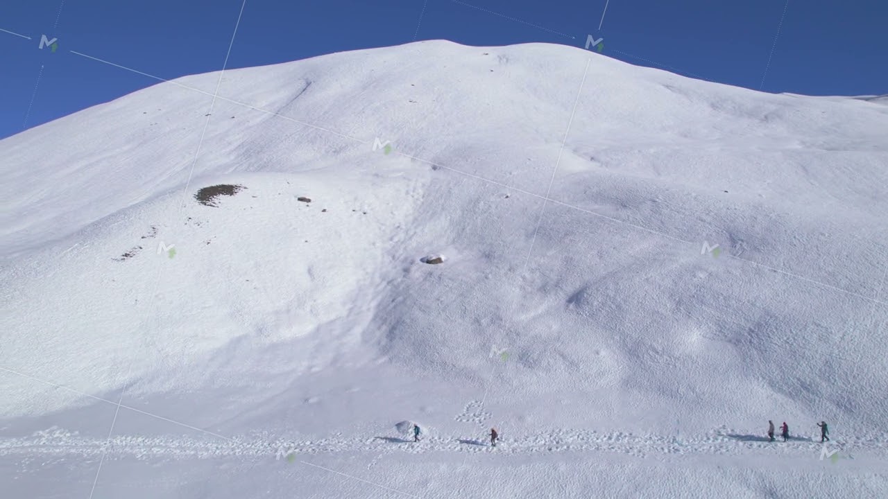 Aerial overhead tracking view of five trekkers group on snowy pathway to Tilicho lake in high