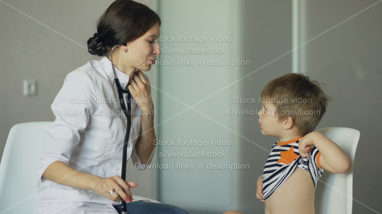 Young woman doctor talking little boy and listening with stethoscope in medical office